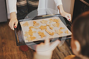 Cute little daughter and mother holding tray with christmas cookies close up in modern kitchen. Cute toddler girl and mom baking