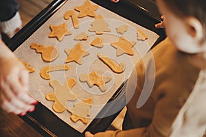 Cute little daughter and mother holding tray with christmas cookies close up in modern kitchen. Cute toddler girl and mom baking