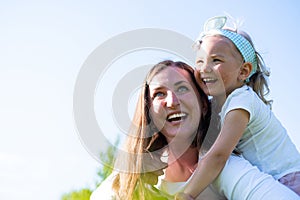 Cute little daughter on a piggy back ride with her mother. Happy mom and girl playing having fun outdoor in park at