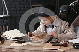 Cute little detective reading old book indoors