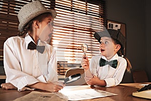 Cute little detectives exploring fingerprints with magnifying glasses at table in office