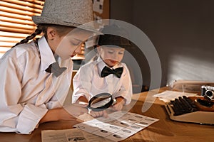 Cute little detectives exploring fingerprints with magnifying glasses at table in office