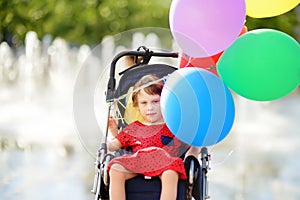 Cute little disabled girl in a wheelchair celebrate birthday or walking in the Park summer. Child cerebral palsy. Inclusion photo
