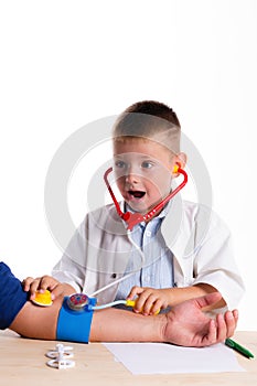 Cute little doctor boy with smile on face sitting at his desk on