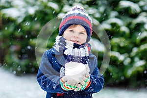 Cute little funny kid boy in colorful winter fashion clothes having fun and playing with snow, outdoors during snowfall