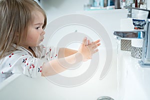 Cute little girl 2-3 years old washing hands with soap and water in bright bathroom