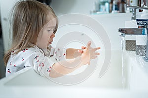 Cute little girl 2-3 years old washing hands with soap and water in bright bathroom