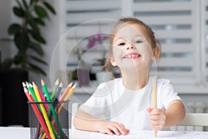 Cute little girl 2-4 in a white t-shirt draws at home with colorful felt-tip pens and pencils