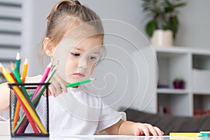 Cute little girl 2-4 in a white t-shirt draws at home with colorful felt-tip pens and pencils