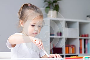 Cute little girl 2-4 in a white t-shirt draws at home with colorful felt-tip pens and pencils