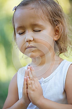 Cute little girl 4 - 5 years old meditating at green summer park in lotus pose