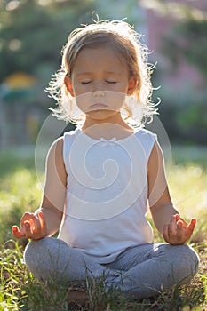 Cute little girl 4 - 5 years old meditating at green summer park in lotus pose