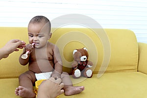 Cute little girl African American baby daughter trying to feed herself with spoon of food, infant kid enjoy eating healthy