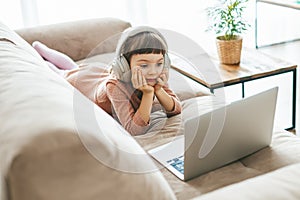 A cute little girl wearing headphones while captivated by the laptop screen. Concept: technology-infused photo