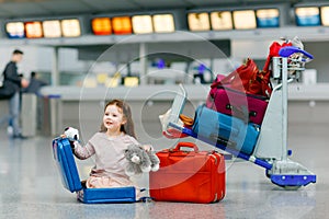 Cute little girl at the airport. Tired child sitting on ground and waiting for delayed flight. Kid playing with toy by