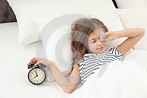 Cute little girl with alarm clock awaking in bed photo