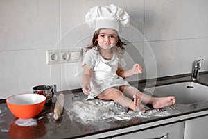 Cute little girl in apron and chef hat is kneading the dough and smiling while baking photo