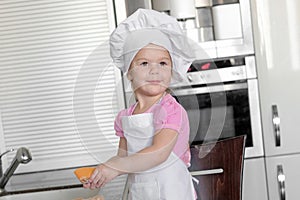 Cute little girl in apron and chef hat is kneading the dough and smiling while baking photo