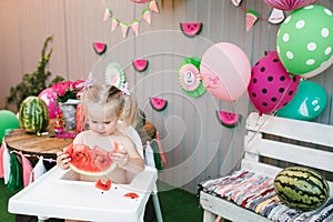 A cute little girl a baby blonde is eating a juicy watermelon in the backyard celebrating a birthday