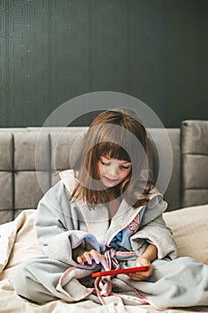 A cute little girl in a bathrobe sitting on a bed, navigating the digital world with focused attention, engrossed in her photo