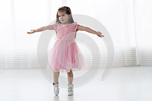 Cute little girl in beautiful dress is dancing at light sunny room.