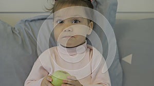 Cute little girl in bed eating apple and posing for the camera