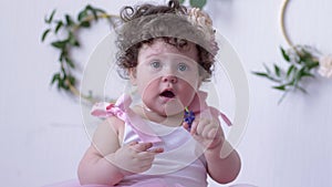 Cute little girl with big eyes and curly hair in pink dress close-up posing in white studio