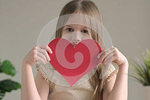 Cute little girl with big paper red heart. Happy child girl with present for Valentines Day, mothers or fathers day. DIY