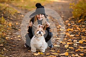 Cute little girl in a black coat with a dog walk in the park. A child is training a dog. Faithful friends of man. Leisure with