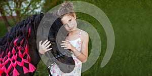 Cute little girl and black pony in a beautiful park. Pretty girl embracing  a pony. Spring or summer time. Copy space for text.