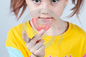 Cute little girl with blond hair is holding a pink dental myofunctional trainer