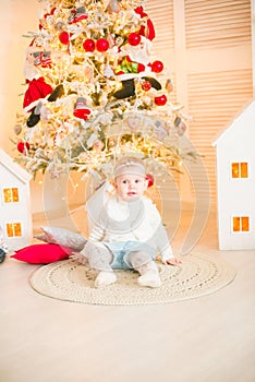 Cute little girl with blond hair plays in a bright room decorated with Christmas garlands near the Christmas tree.
