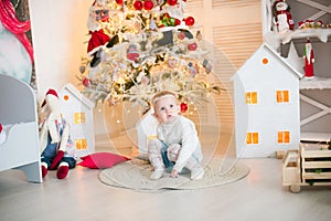 Cute little girl with blond hair plays in a bright room decorated with Christmas garlands near the Christmas tree.