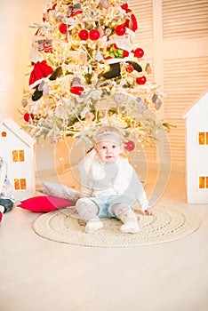 Cute little girl with blond hair plays in a bright room decorated with Christmas garlands near the Christmas tree.