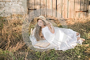 Cute little girl with blond long hair in a summer field at sunset with a white dress with a straw hat