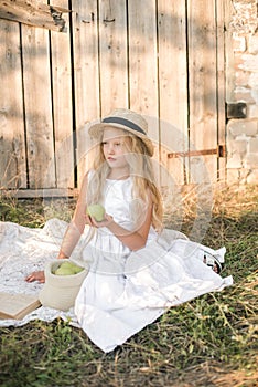 Cute little girl with blond long hair in a summer field at sunset with a white dress with a straw hat