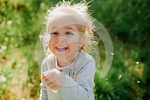 Cute little girl blow on a dandelion on spring sunny background