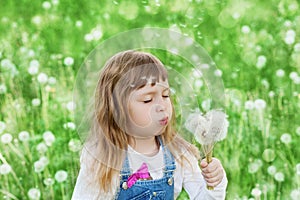 Cute little girl blowing dandelion on the flower meadow, happy childhood concept