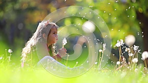 Cute little girl blowing  dandelions in autumn park. Wishes, dreams, playtime.