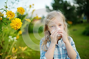 Cute little girl blowing her nose by beautiful yellow coneflowers on summer day. Allergy and asthma issues in small kids. photo