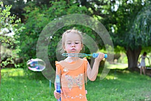 Cute little girl blowing soap bubbles in nature