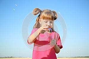 Cute little girl blowing soap bubbles on sunny day