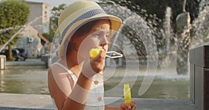 Cute little girl blows soap bubbles on the background of a fountain.