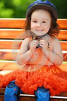 Cute little girl in blue helmet sits on bench at