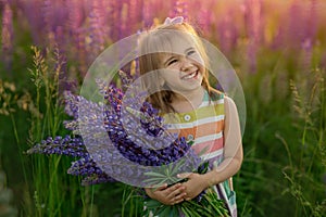 A cute little girl with a bouquet of lupines in a field of purple flowers smiles sweetly looking up. copy space