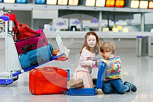 Cute little girl and boy at airport. Tired children, siblings sitting on ground and waiting for delayed flight. Kids