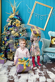 Cute little girl and boy are smiling and holding gifts under the Christmas tree. Brother and sister unpack gift boxes on Christmas