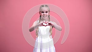 Cute little girl with braids showing heart gesture, charity, children adoption