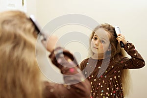 Cute little girl brushing hair while looking in the mirror