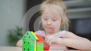 a cute little girl builds houses from a colorful wooden construction set.